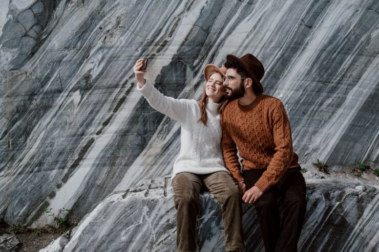 Couple sitting on granite rocks, wearing panama hats, taking a selfie